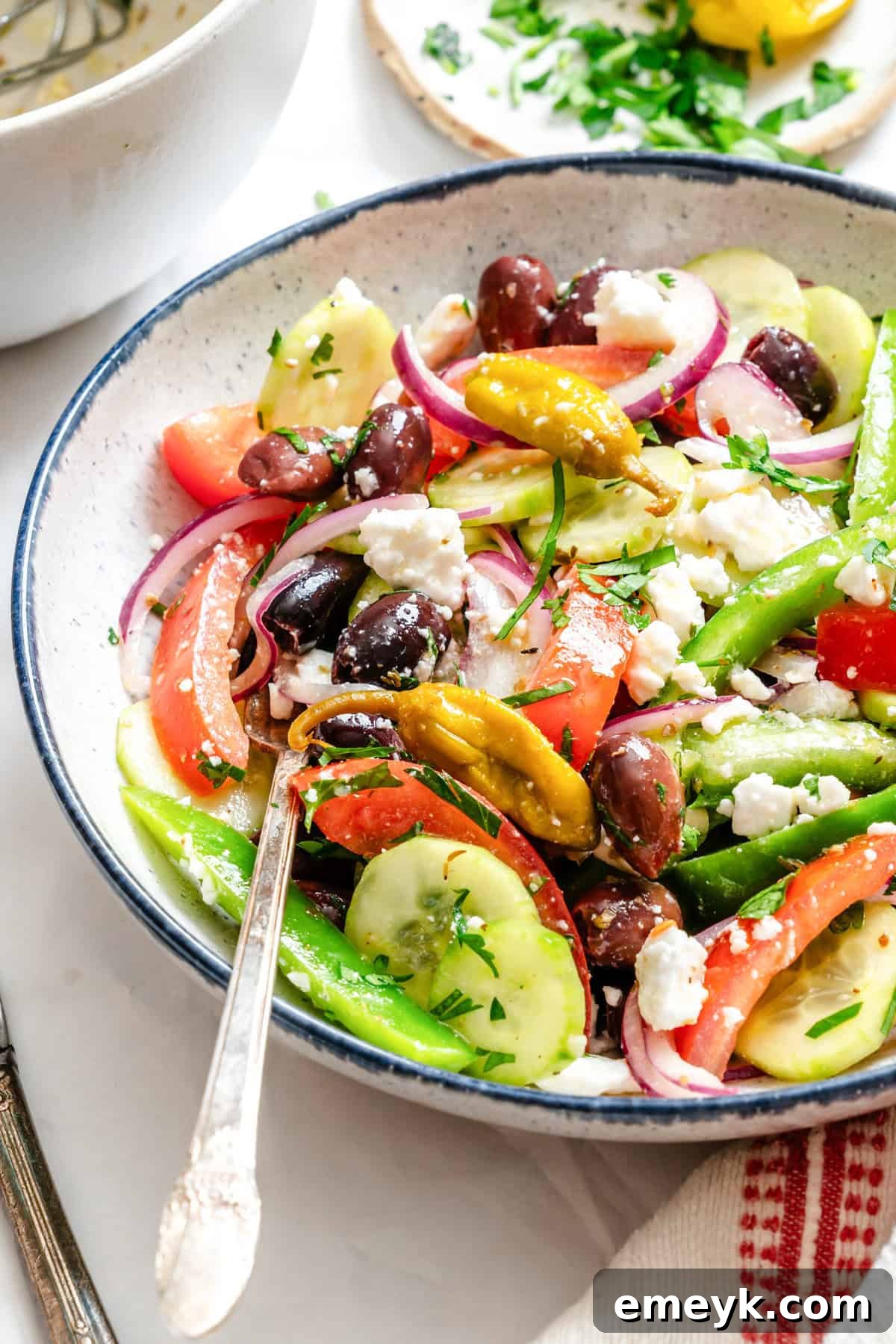 A vibrant Greek Village Salad, Horiatiki, artfully arranged in a white bowl with a fork ready to serve.
