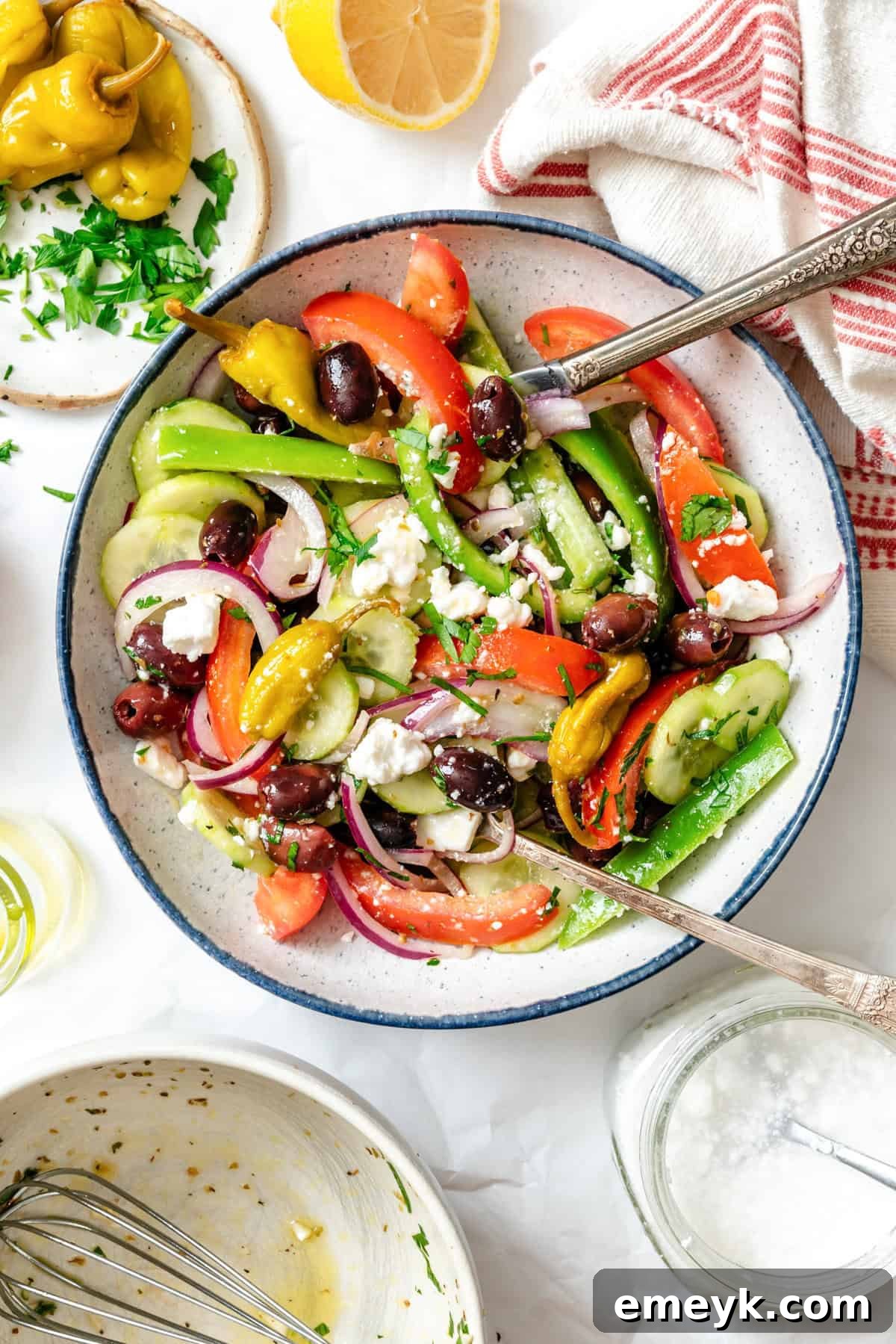 A bowl of fresh Greek Village Salad with a blue rim, served with a fork, highlighting the vibrant colors and textures.