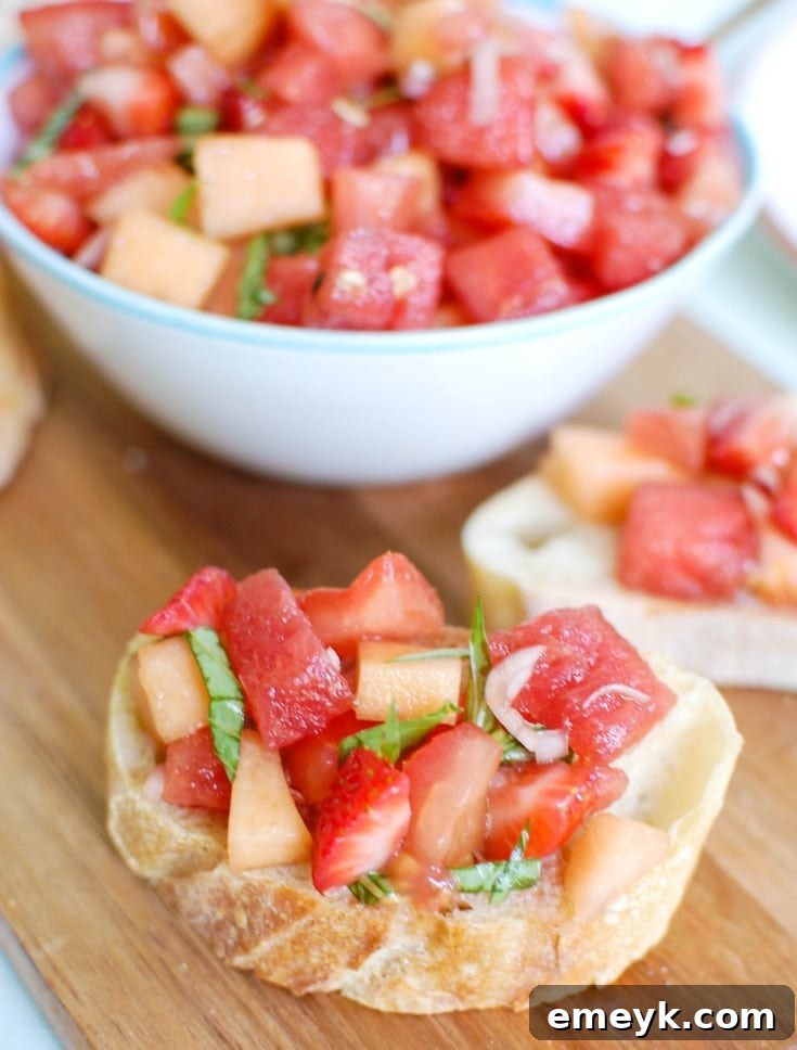 A close-up of fresh, diced ingredients for Berry Melon Bruschetta, including tomatoes, watermelon, cantaloupe, strawberries, and basil.