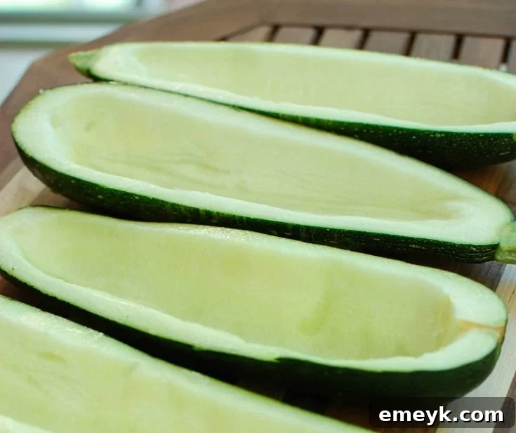 Zucchini halves being scooped out, ready for the savory Mediterranean filling.