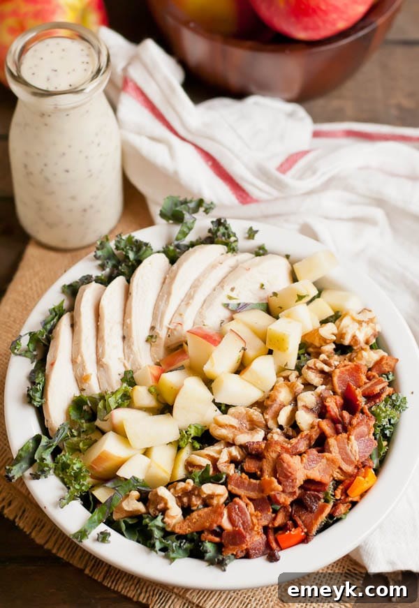 A hearty chicken, apple, bacon, and kale salad in a bowl, showing colorful ingredients and a light dressing.