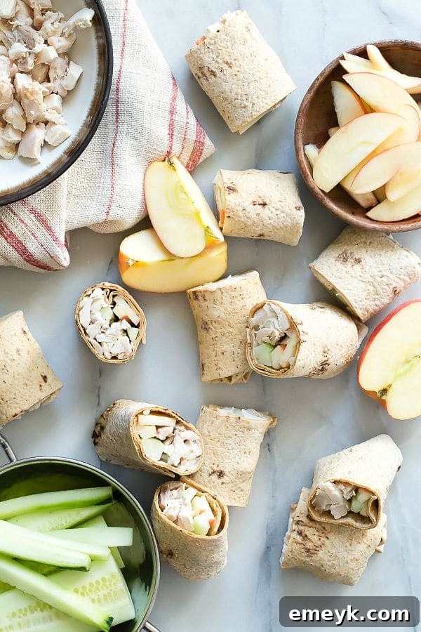 Rolled cucumber apple chicken wraps, sliced in half to show the filling, with fresh vegetables.