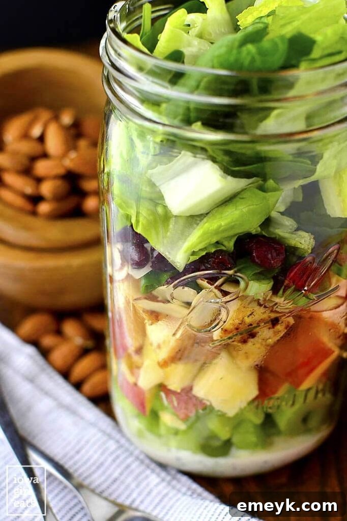 Layered almond, cranberry, and apple mason jar salads, showing distinct layers of greens, fruit, and dressing.