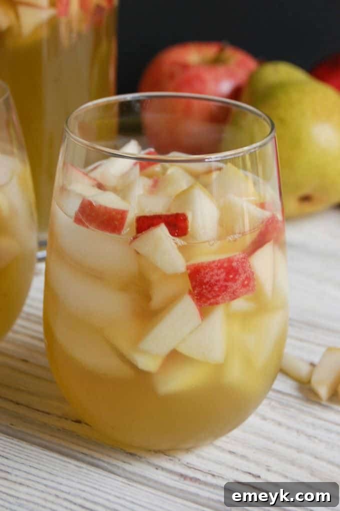 A glass pitcher filled with Sparkling Apple Pear Sangria, garnished with fresh apple slices, pear slices, and cranberries.