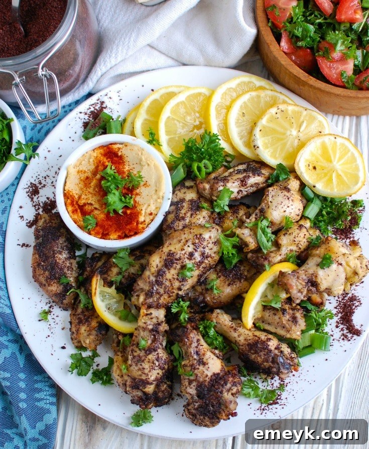 A flat lay of fresh ingredients for Sumac Lemon Baked Chicken Wings, including raw chicken wings, whole lemons, dried sumac spice, garlic cloves, and a bottle of olive oil.