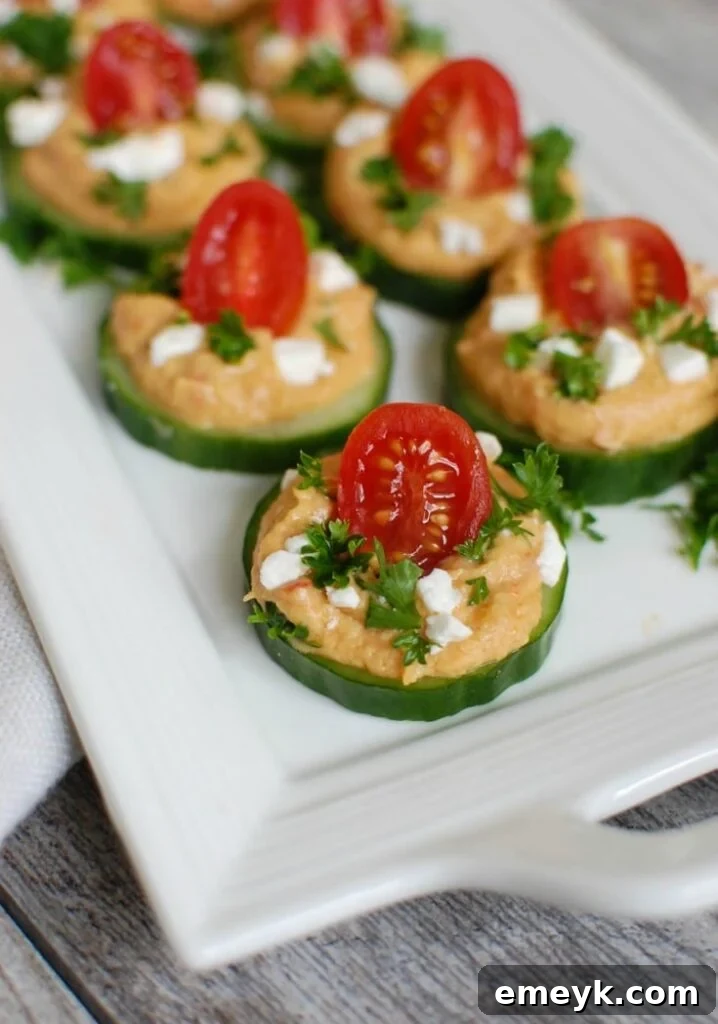 Refreshing Cucumber Hummus Bites, perfect as an appetizer, adorned with roasted red pepper hummus, tomatoes, feta cheese, and fresh parsley.