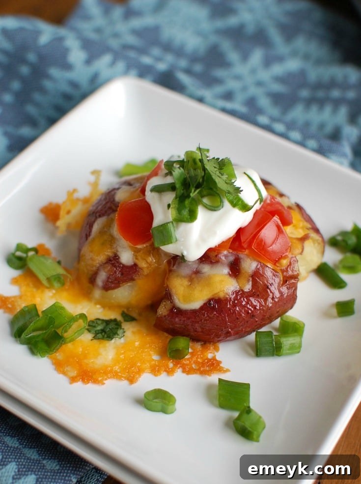 Close-up of golden brown Loaded Smashed Potatoes topped with melted cheese, sour cream, fresh diced tomatoes, and green onions, ready to be served.