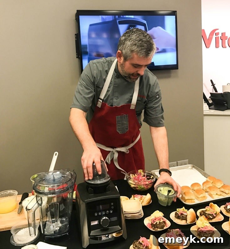 A professional Vitamix blender in action, making a vibrant drink, with fresh ingredients nearby.