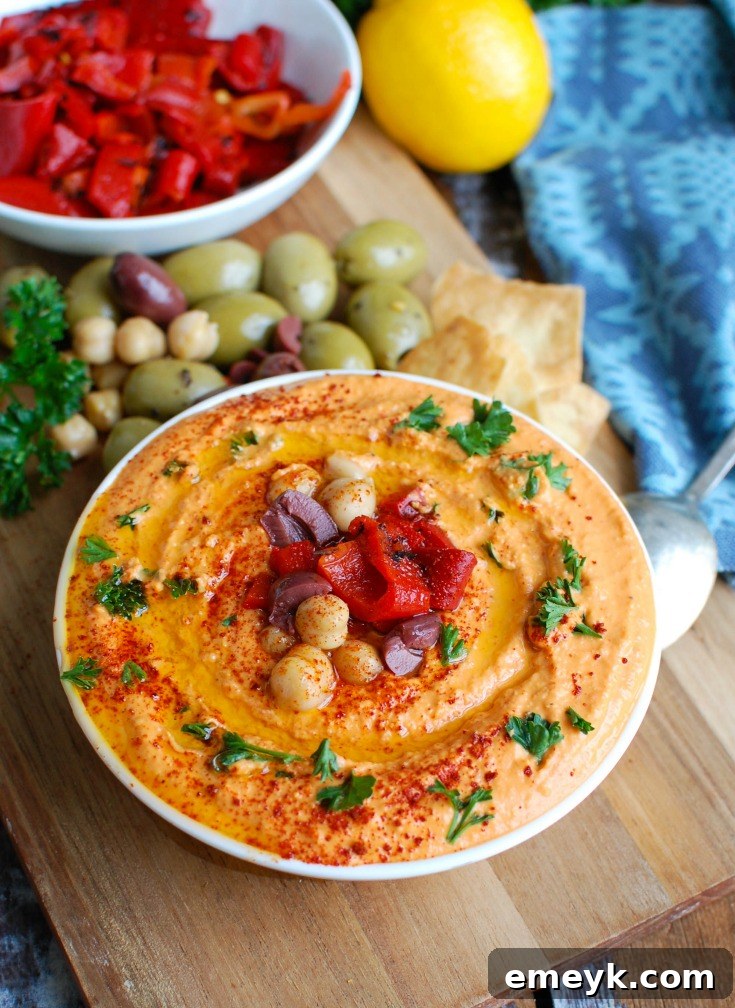 A smooth and creamy bowl of Roasted Red Pepper Greek Yogurt Hummus garnished with fresh parsley and a drizzle of olive oil, ready to be served with pita and vegetables.