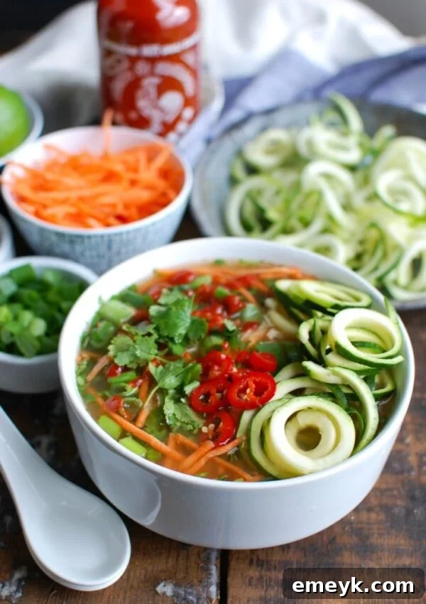 A spoon dipping into a bowl of Spicy Chicken Zoodle Soup, highlighting the fresh garnishes.