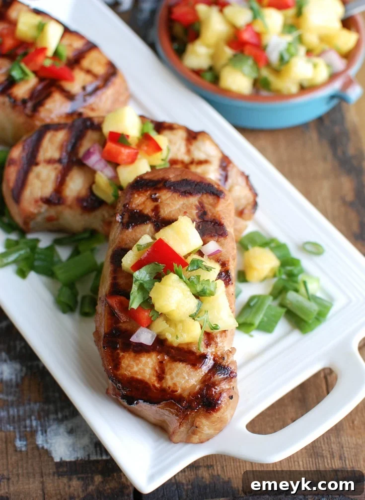 Aloha Grilled Pork Chops 2 Grilled Hawaiian Pork Chops on a white platter, ready to be served, showcasing their beautiful char marks and vibrant pineapple salsa.