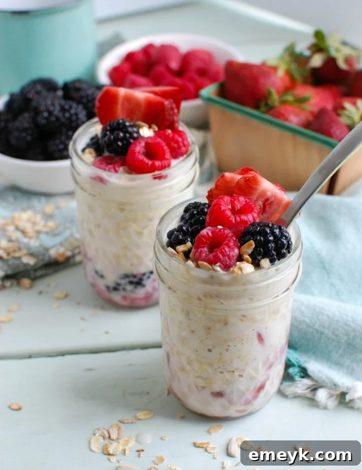 All the fresh ingredients laid out for Overnight Triple Berry Oatmeal: rolled oats, a bowl of mixed blueberries, raspberries, and strawberries, a carton of milk, a container of Greek yogurt, and a bottle of vanilla extract, all ready for preparation.