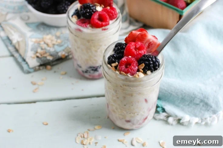 A top-down view of two mason jars, one containing the layered berries and oats before soaking, and the other showing the finished Overnight Triple Berry Oatmeal, garnished with extra fresh berries and chia seeds, highlighting the simplicity and beauty of the preparation process.