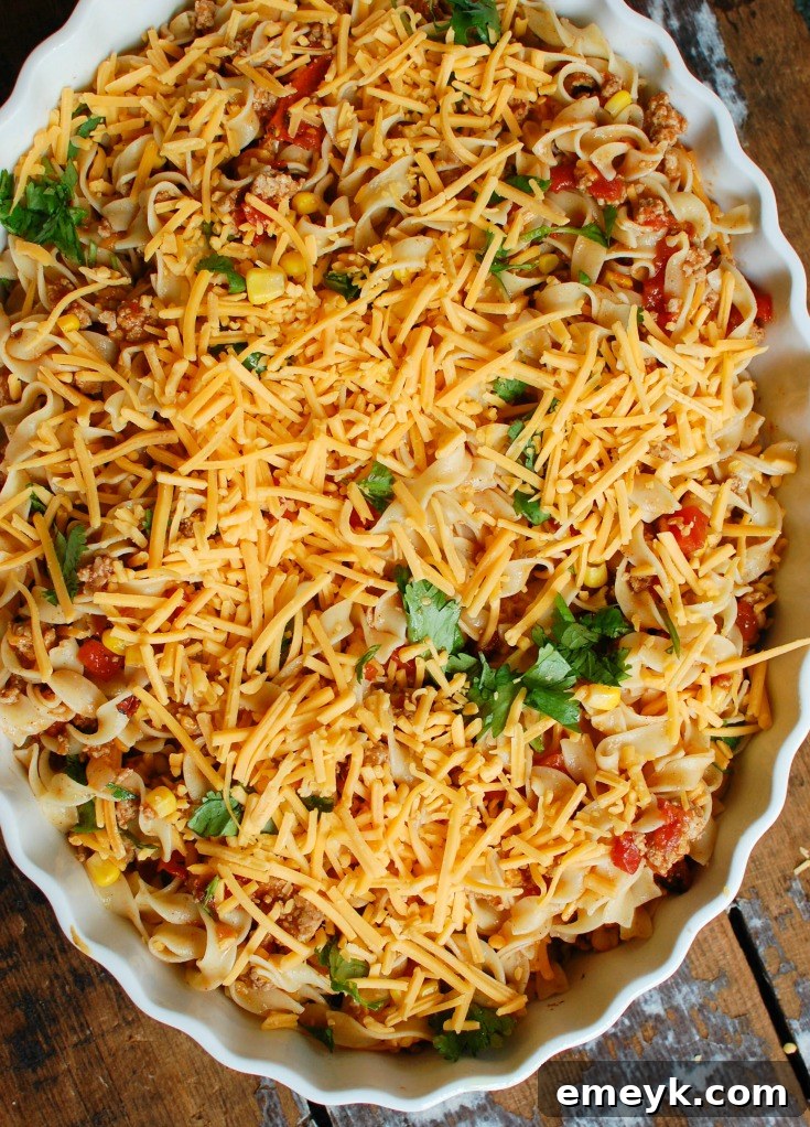 The assembled Mexican Noodle Casserole in a baking dish, topped with shredded cheese and cilantro, ready for the oven.