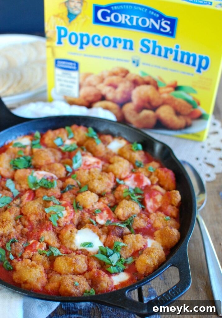 A close-up shot of Tomato Basil Mozzarella Popcorn Shrimp Bites on a wooden serving board, featuring crispy shrimp covered in melted mozzarella, vibrant red tomato sauce, and fresh green basil leaves. Crackers are arranged around the dish, suggesting a perfect appetizer for sharing.