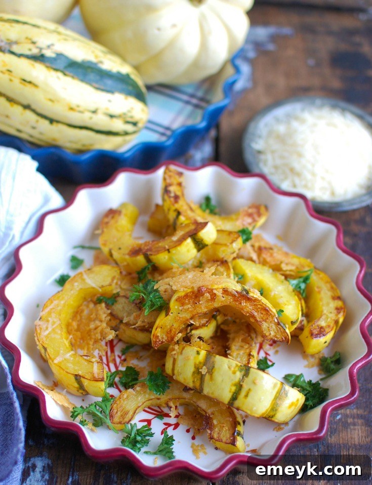 Parmesan Roasted Delicata 4 Close-up of roasted delicata squash slices on a baking sheet, with melted Parmesan cheese and fresh parsley garnish.