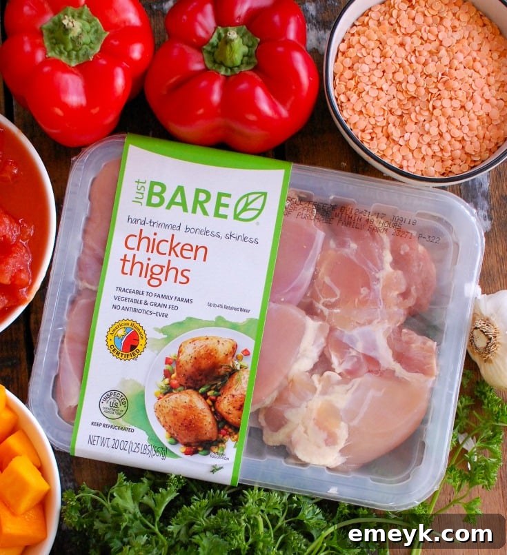 A collection of fresh ingredients laid out on a wooden board, ready for Slow Cooker Moroccan Chicken Soup, including chicken thighs, colorful vegetables, a mix of vibrant spices, and red lentils.
