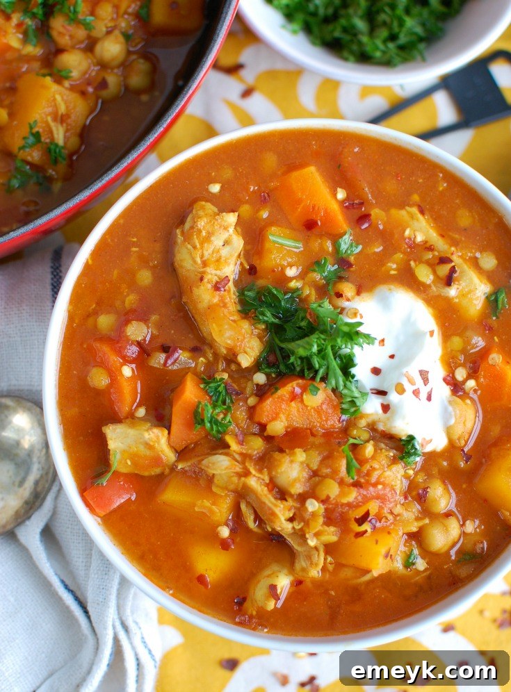 A close-up shot of Slow Cooker Moroccan Chicken Soup in a white bowl, generously garnished with a dollop of creamy Greek yogurt and fresh green herbs like cilantro and parsley.