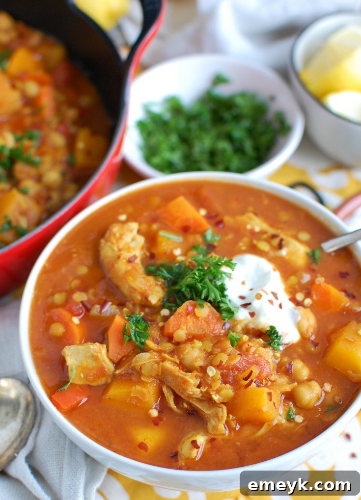 A close-up view of a bowl of Slow Cooker Moroccan Chicken Soup, showcasing its rich texture, vibrant colors, and tender ingredients, with a spoon poised to enjoy.