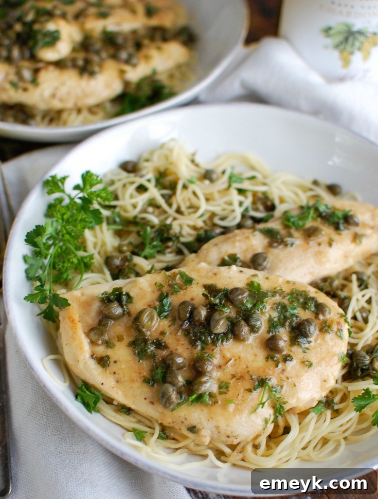 Zesty Lemon Caper Chicken 2 Golden brown Chicken Piccata served in a white bowl, generously drizzled with lemon-caper sauce and garnished with fresh parsley.