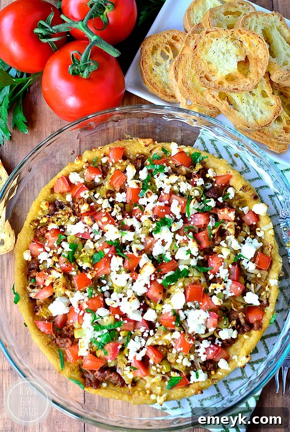 Store-bought hummus is spread into a pie pan then topped with browned sausage, sauteed leeks, chopped tomatoes, and crumbled feta cheese with crostini made from baguettes