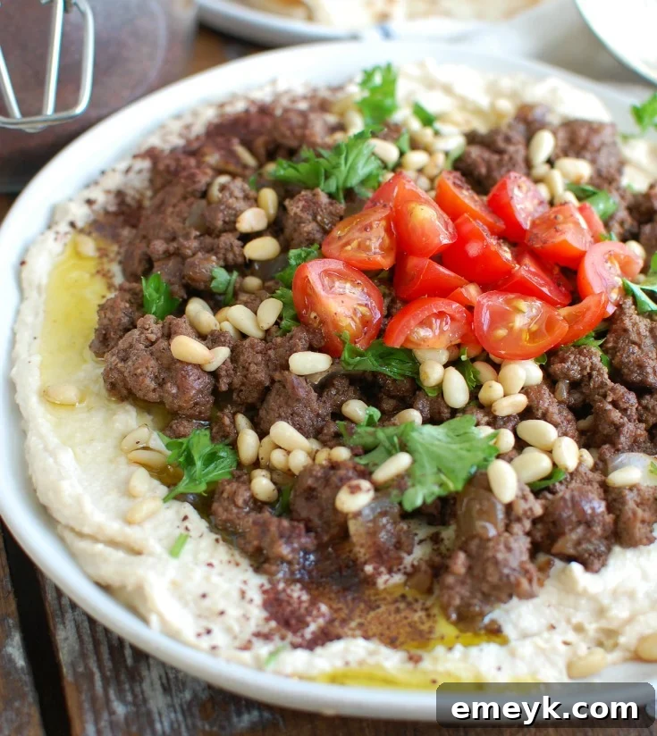 Creamy Hummus with Spiced Beef and Toasted Pine Nuts, garnished with fresh tomatoes and parsley, served as an appetizer or meal.