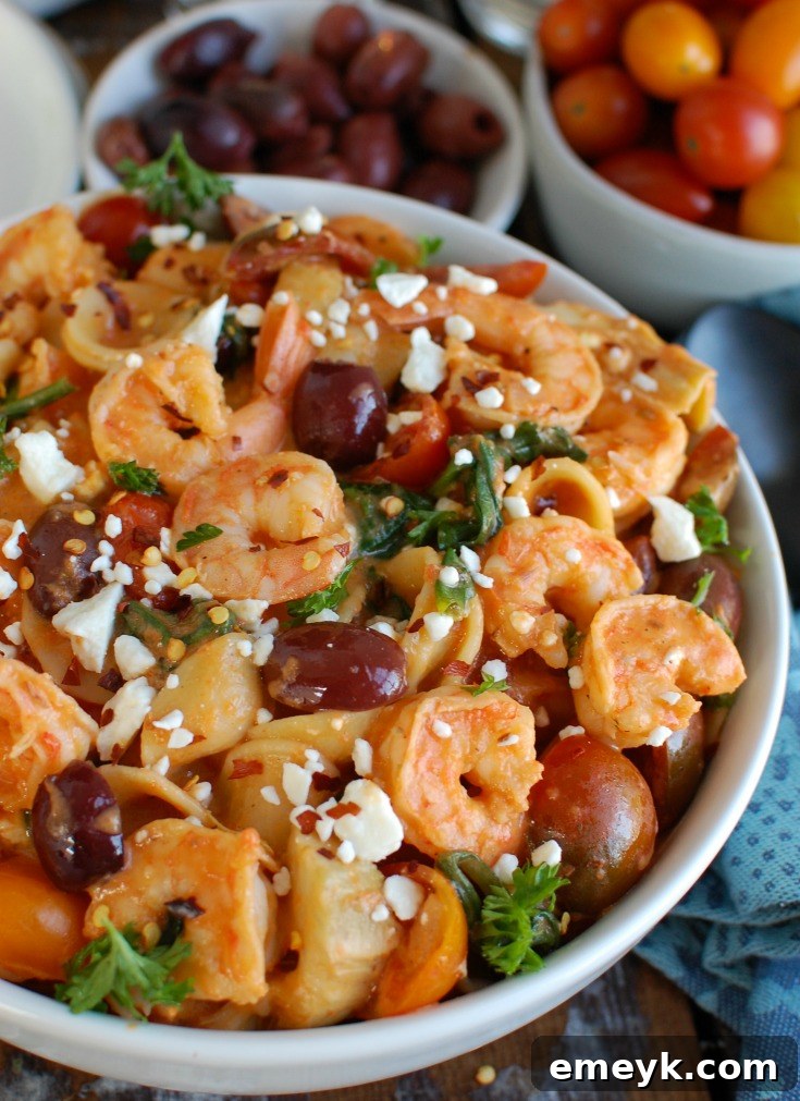 A close-up shot of One Pot Mediterranean Shrimp Pasta in a rustic bowl, showcasing the vibrant red pepper sauce, pink shrimp, and colorful Mediterranean ingredients.