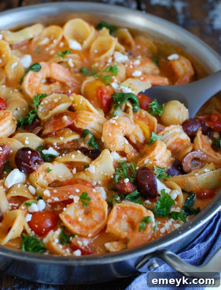 Various fresh ingredients for Mediterranean shrimp pasta laid out on a wooden board, including red onion, garlic, uncooked shrimp, cherry tomatoes, kalamata olives, and artichoke hearts.
