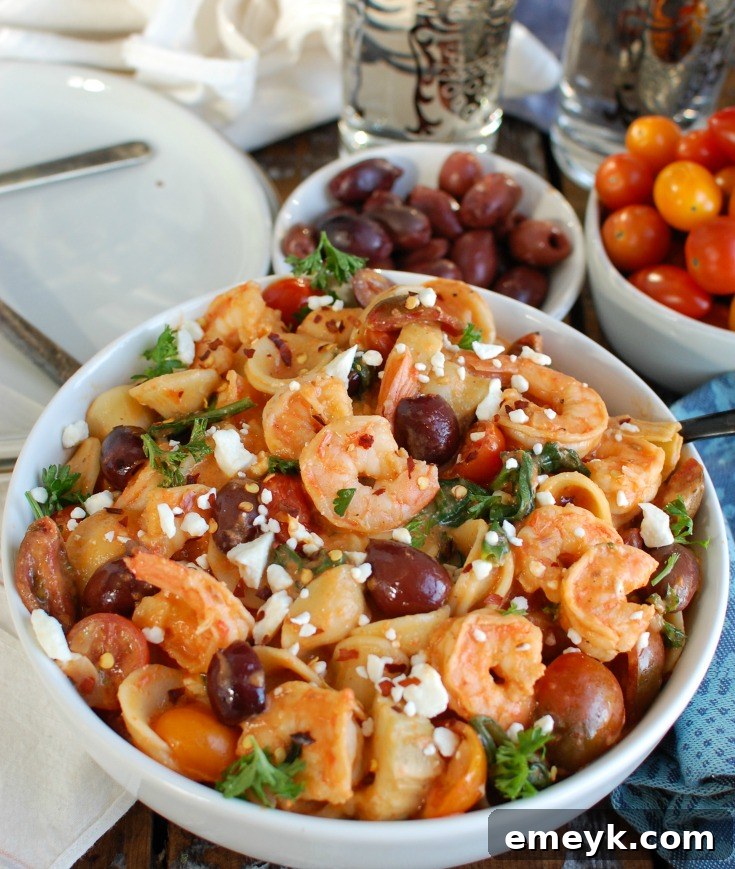 A large pot of One Pot Mediterranean Shrimp Pasta cooking on the stove, with ingredients like pasta, shrimp, spinach, and the red pepper sauce visible.