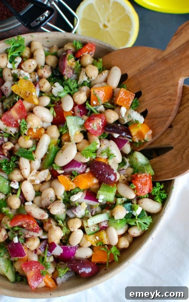 Close-up of Mediterranean Bean Salad being served with tongs from a large bowl.