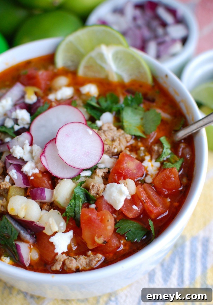 A close-up of Slow Cooker Pork Pozole in a white bowl, beautifully garnished with fresh sliced radishes and a bright lime wedge, ready to be served and enjoyed.