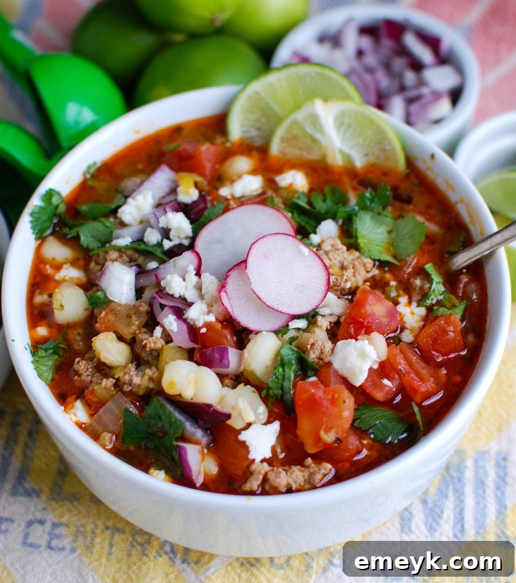 A ladle scooping rich Slow Cooker Pork Pozole from a white bowl, highlighting the tender pork, plump hominy, and savory broth.