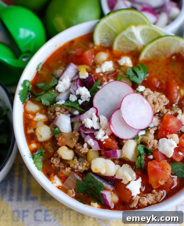 Slow Cooker Pork Pozole served in a white bowl, accompanied by fresh lime wedges, ready for customization and enjoyment.