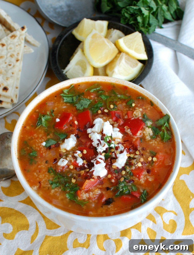 Close-up of Tomato Red Pepper Bulgur Soup, garnished generously with crumbled feta cheese and fresh herbs.