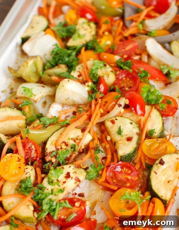 Close-up of roasted vegetables on a sheet pan, showing colorful bell peppers, zucchini, and onions.