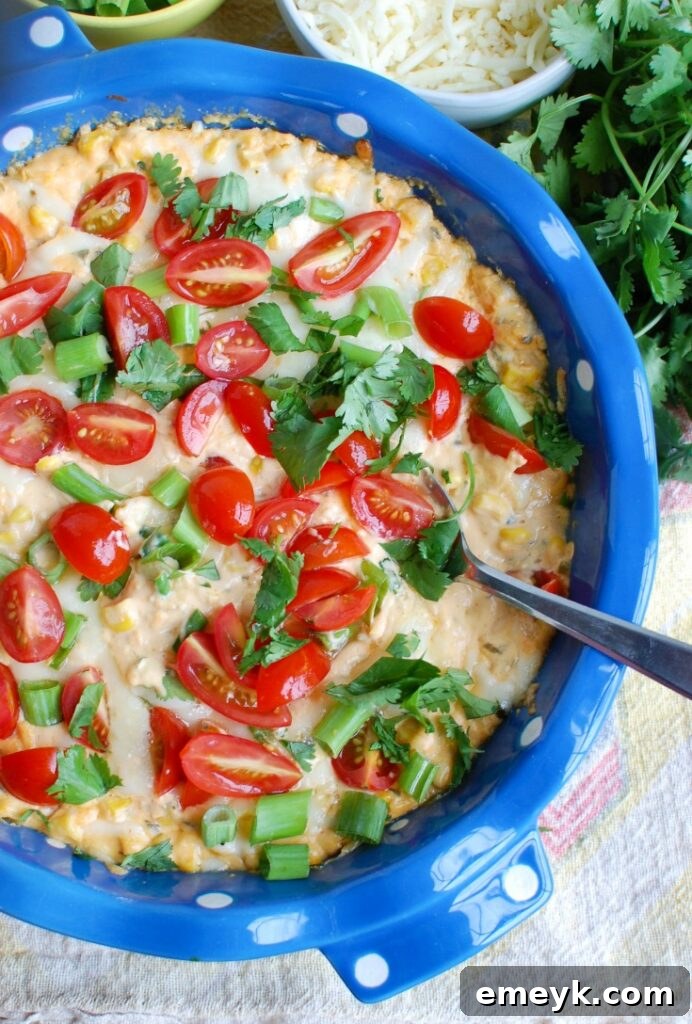 Baked Sriracha Sweet Corn Dip garnished with fresh cilantro and tomatoes, served with tortilla chips, close-up shot revealing melted cheese and corn kernels.