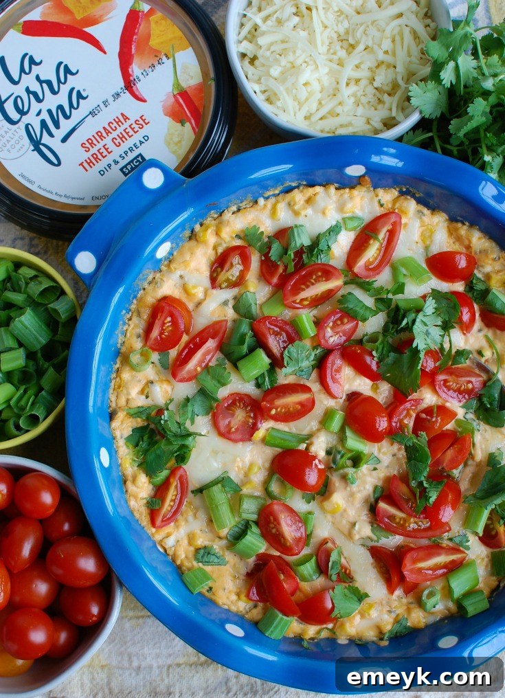 Close-up of Baked Sriracha Sweet Corn Dip in a blue ceramic dish, showing bubbling cheese and a rich texture, ready to be scooped.