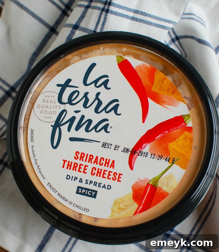 Variety of La Terra Fina Sriracha Three Cheese Dip containers on a wooden board, showcasing product branding and ingredients.
