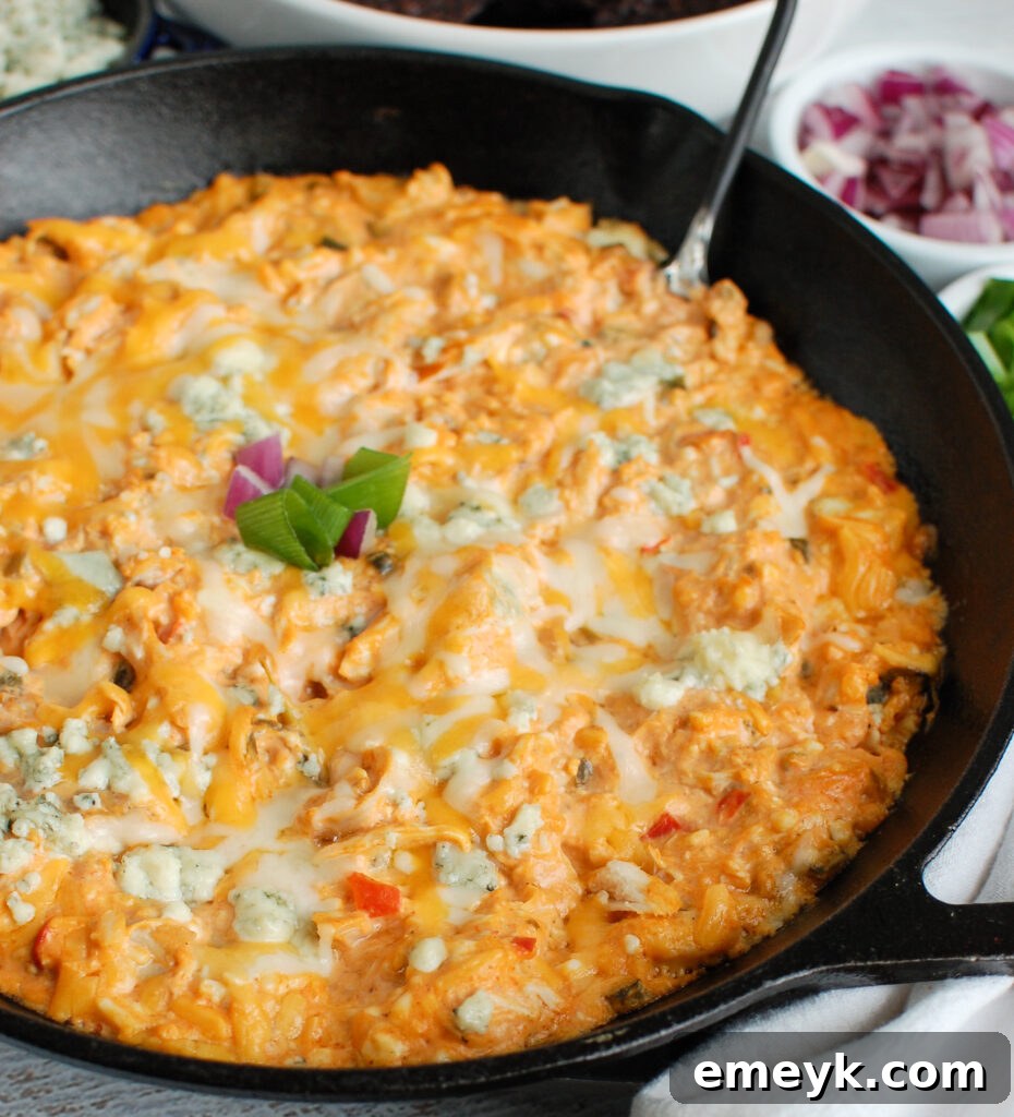 Buffalo Chicken Queso Cheese Dip bubbling in a black cast iron skillet, garnished with fresh herbs.