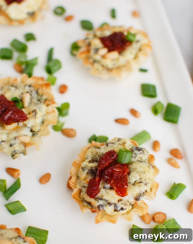 Crispy Spinach Artichoke Sun-dried Tomato Phyllo Bites on a white serving plate, garnished with fresh parsley.