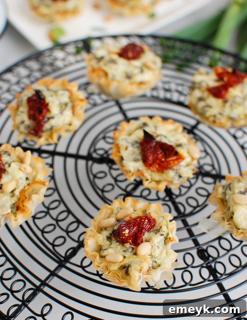 Freshly baked Spinach Artichoke Sun-dried Tomato Phyllo Bites cooling on a wire rack, showing golden edges.