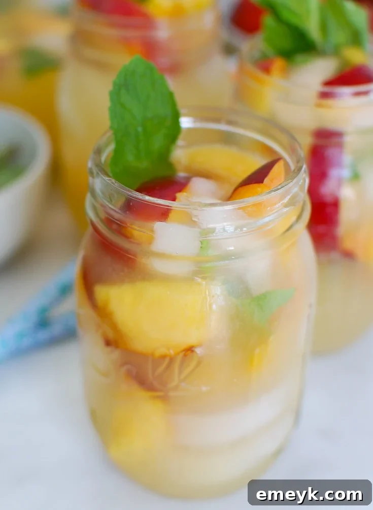 A mason jar filled with Sparkling Peach Lemonade, garnished with fresh mint and peach slices, perfect for summer