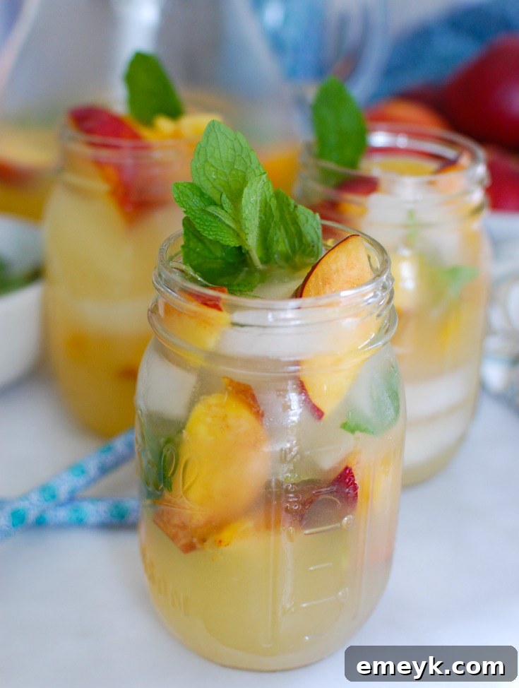 Three glasses of Sparkling Peach Lemonade with ice, peach slices, and mint garnish