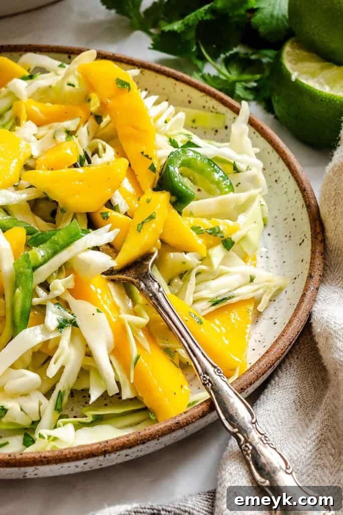 A close-up of Easy Mango Cabbage Coleslaw in a bowl with a fork, showing its enticing texture and fresh components.