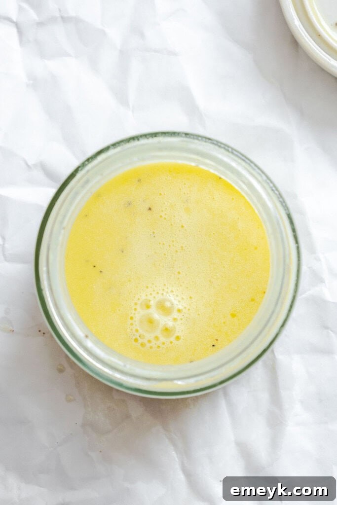 Pouring the homemade dressing over the mixed cabbage and mango in a bowl, preparing to toss.