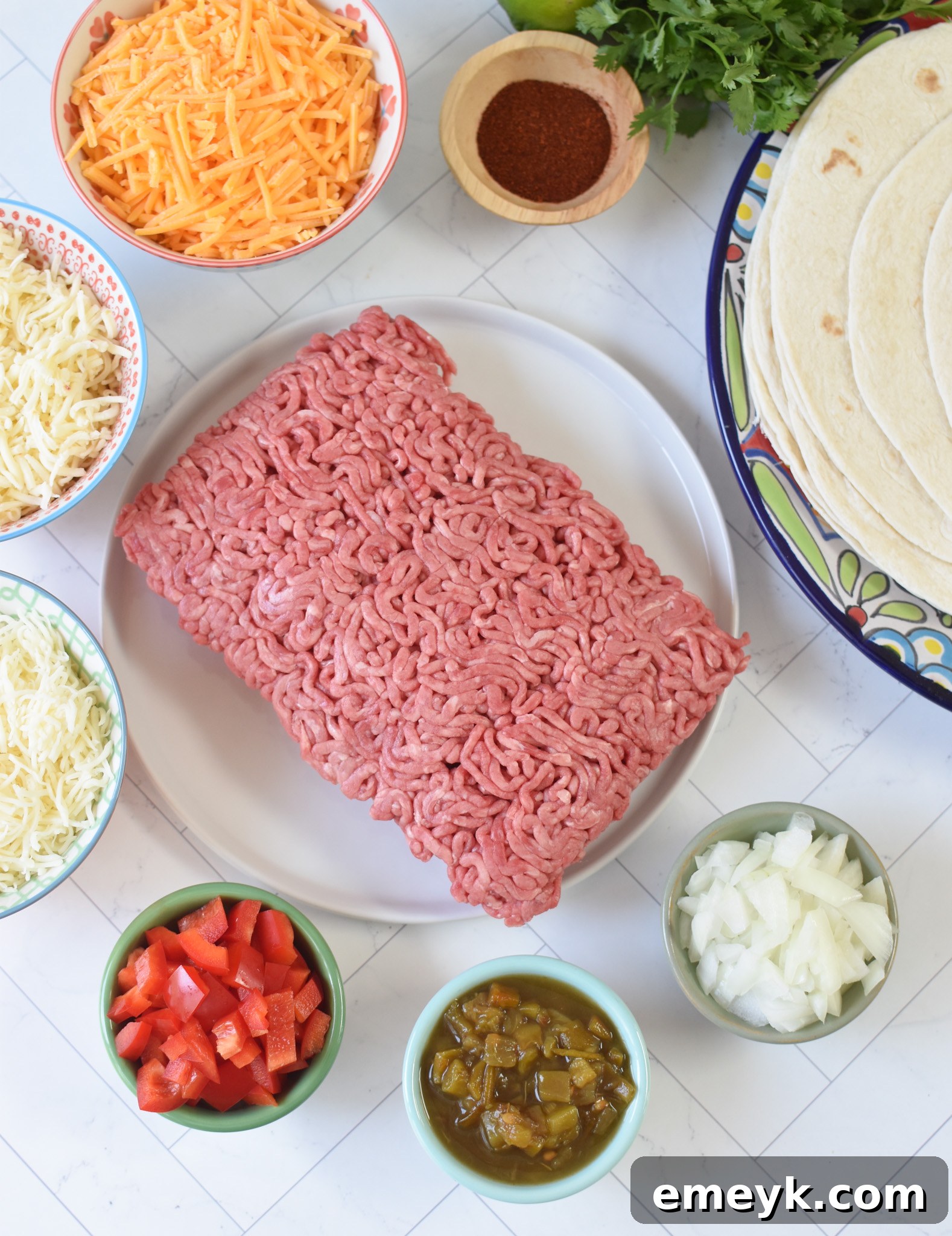 Homestyle Beef Enchiladas 3 A flat lay photograph showcasing all the fresh ingredients needed to make homemade Beef Enchiladas, including ground beef, bell peppers, onions, cheese, tortillas, and various spices.