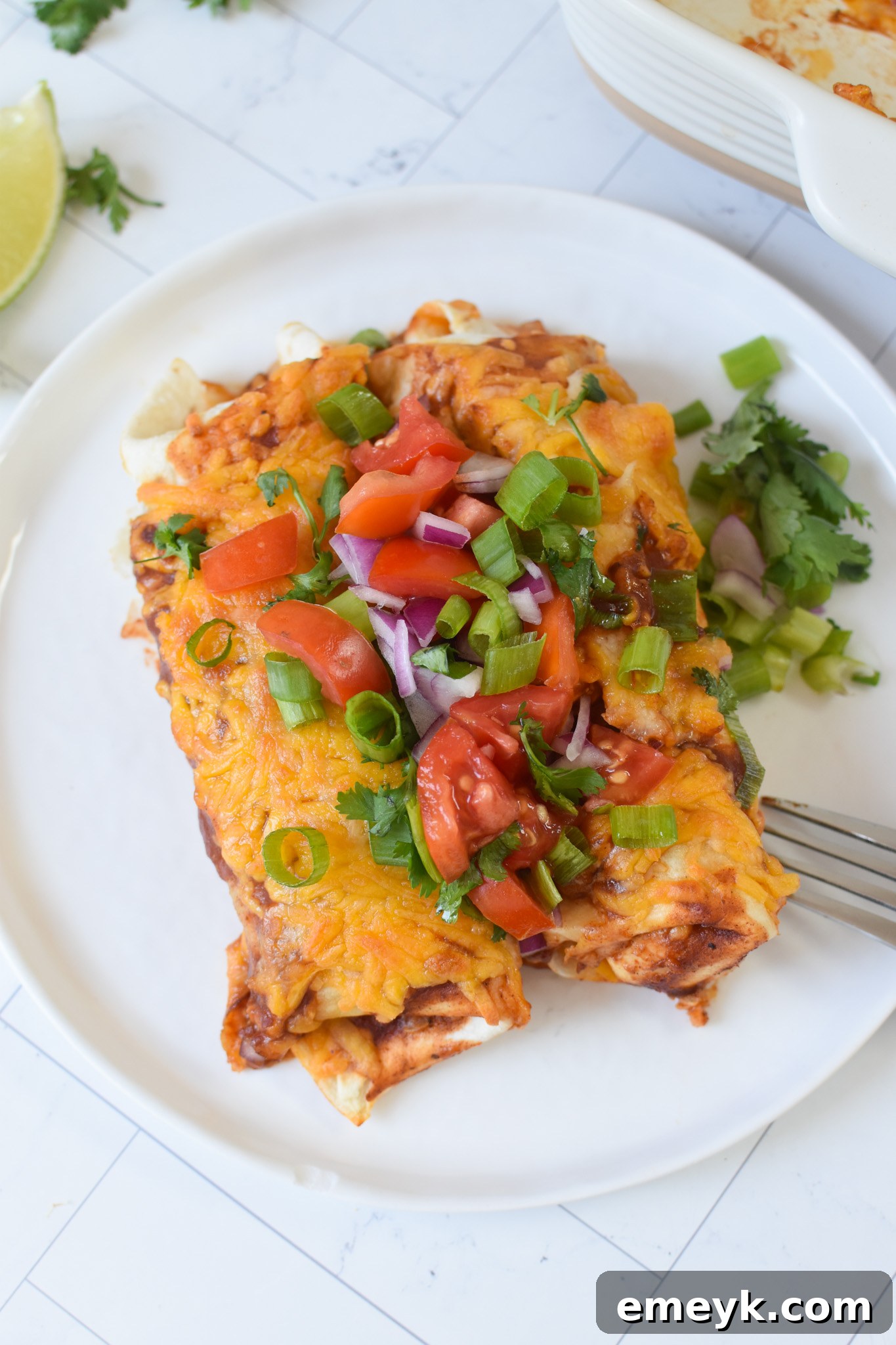 Homestyle Beef Enchiladas 5 A single serving of Beef Enchiladas on a white plate, topped with fresh avocado slices, sour cream, and cilantro, served with a side of Mexican rice.