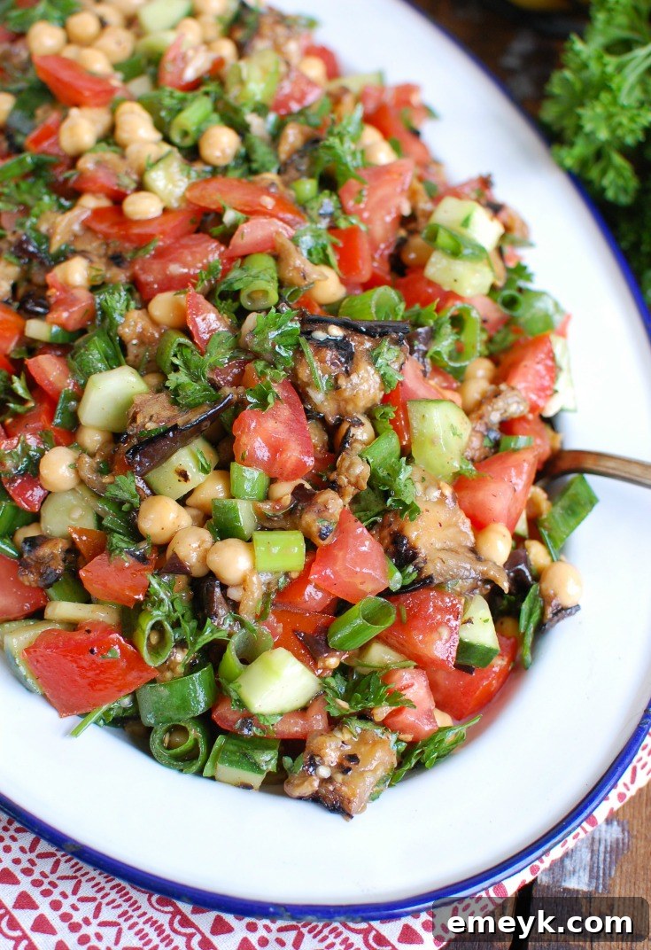 Large white platter overflowing with Mediterranean Eggplant Chickpea Salad, garnished with fresh herbs