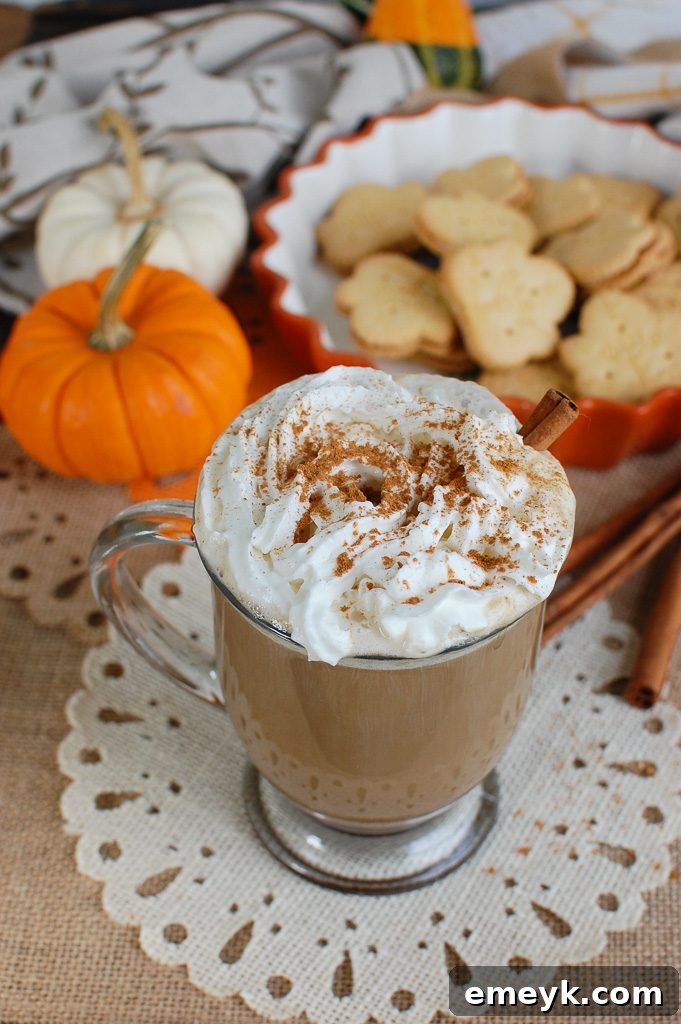 Fall's Signature Sip 3 Two mugs of homemade Pumpkin Spice Latte, one topped with generous whipped cream and spice, resting on a rustic wooden surface with fall decorations.
