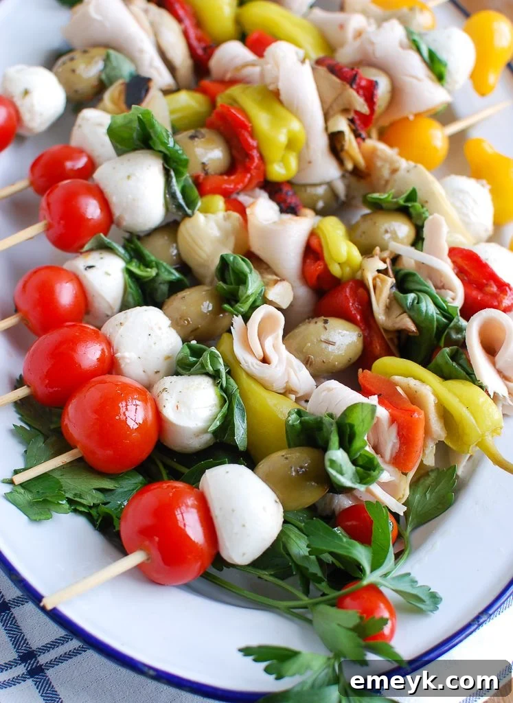 Sunny Mediterranean Skewers 2 Vibrant Mediterranean Antipasto Skewers on a white serving plate, featuring turkey, olives, mozzarella, and vegetables